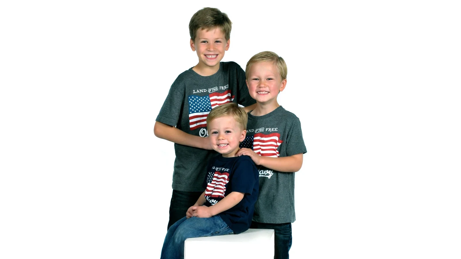 Three smiling children wearing American flag shirts against a white background.