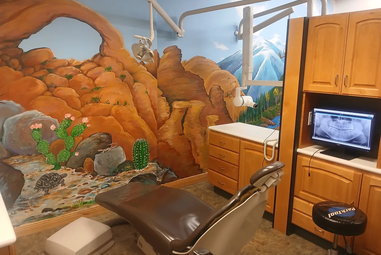 Treatment room with a hand-painted red-rock arch and desert mural, and a panoramic X-ray on the monitor.